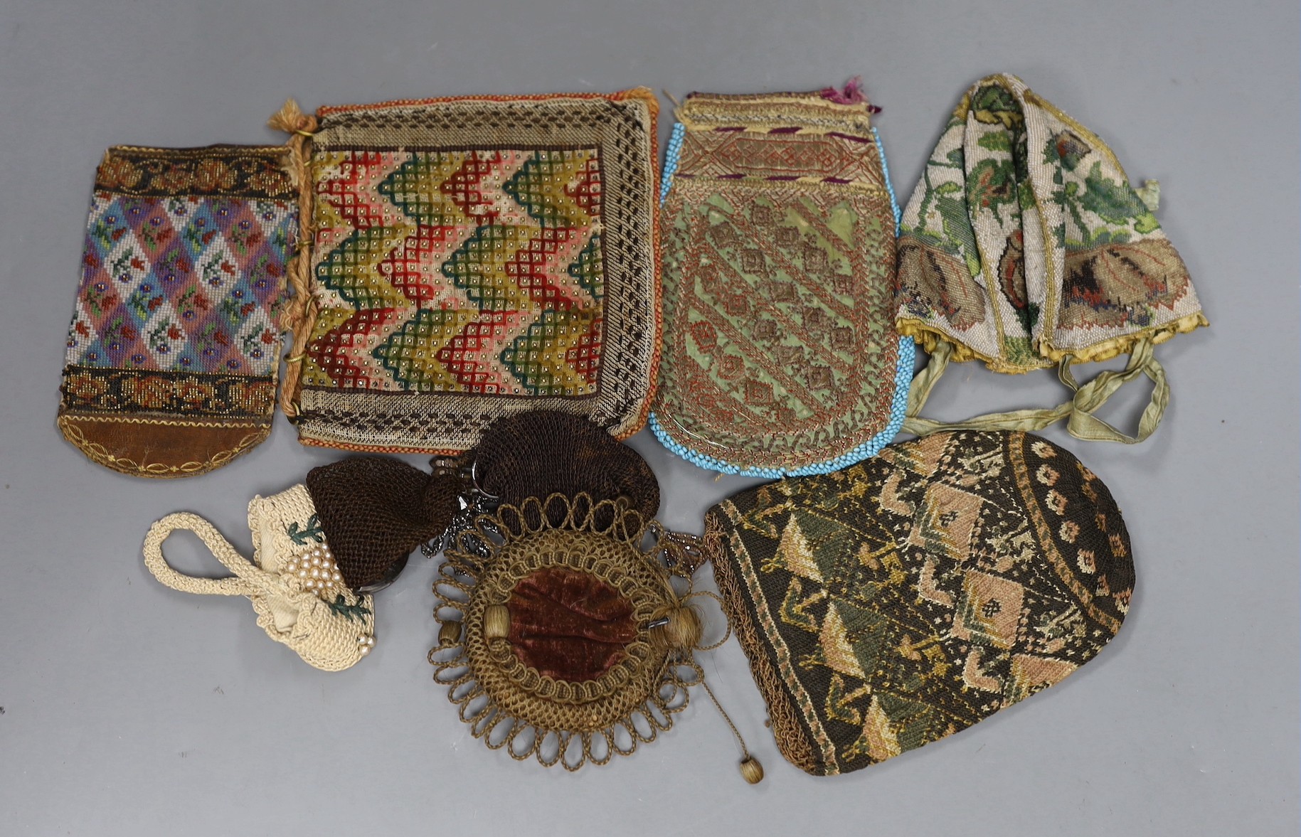 An early 19th century , possibly earlier, four sectioned floral bead worked reticule with ribbon handles, a hair and velvet pin cushion, a North African metallic embroidered bag, a similar bead and leather container, a k